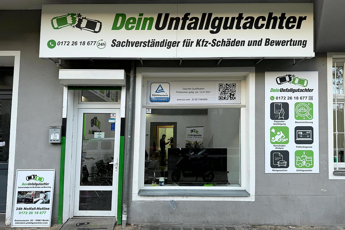 Beleuchtetes Ladenschild von Dein Unfallgutachter in der Gneisenaustraße 55 mit TÜV-Rheinland-Siegel und Leistungsübersicht im Schaufenster