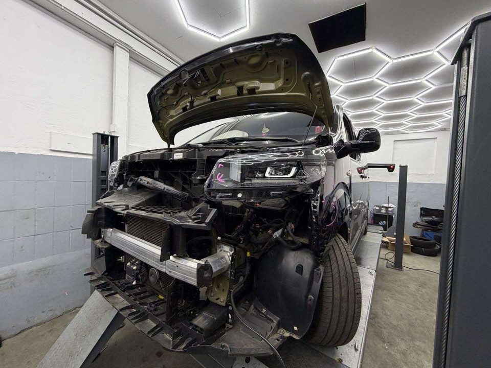 Derselbe Van in der Werkstatt mit abgebautem Stoßfänger: freiliegende Träger, Halter und Kabel hinter der Front